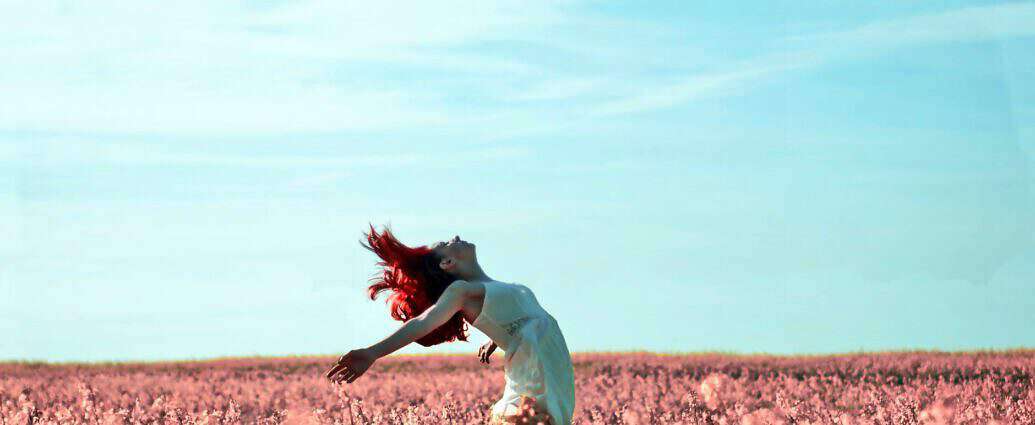 Eine junge Frau steht in einer Blumenwiese und streckt sich leidenschaftlich der Sonne entgegen.