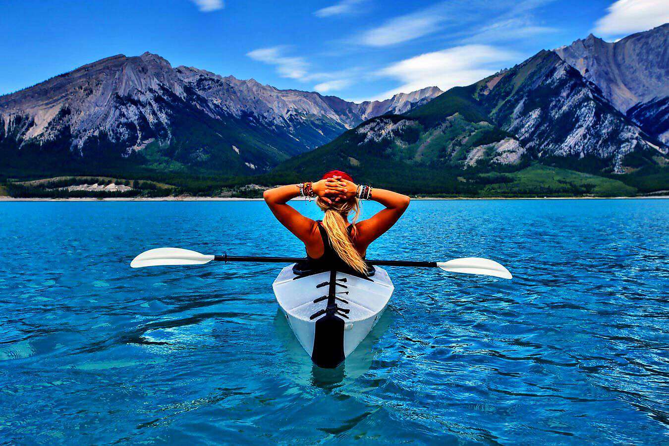Eine junge Frau schwimmt in einem Kajak auf einem See; im Vordergrund sind die Berge zu sehen.