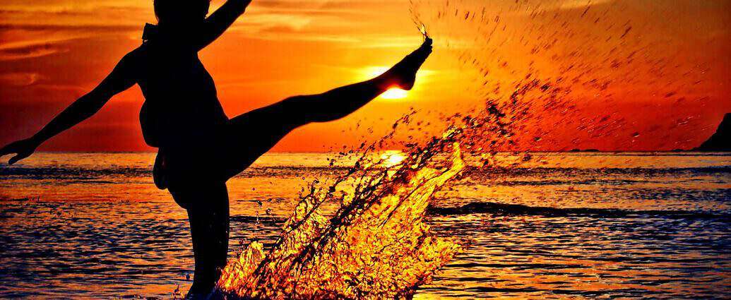 Eine junge Frau steht im Wasser und spritzt mit ihrem Bein Wasser in die Luft.