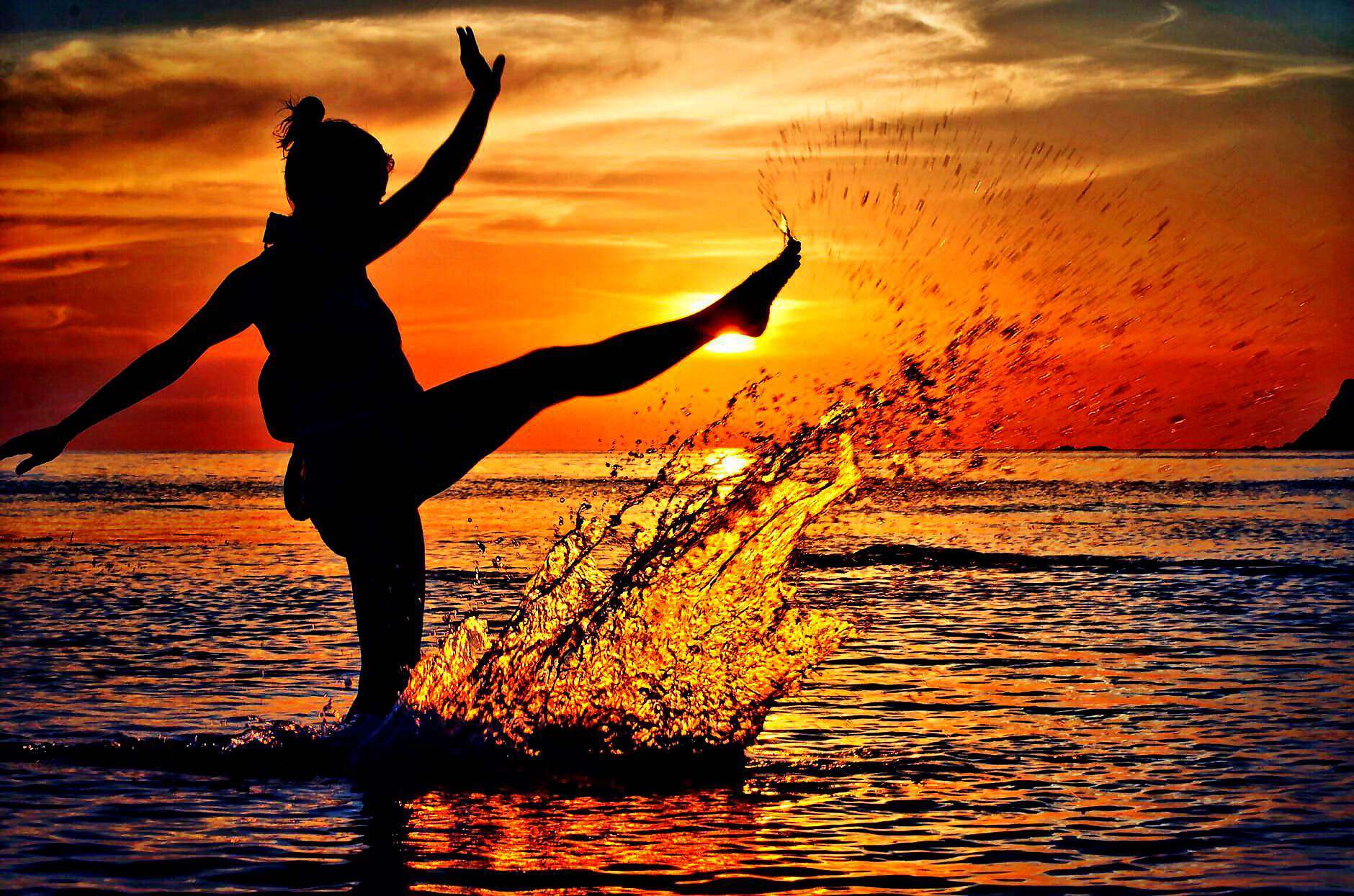 Eine junge Frau steht im Wasser und spritzt mit ihrem Bein Wasser in die Luft.