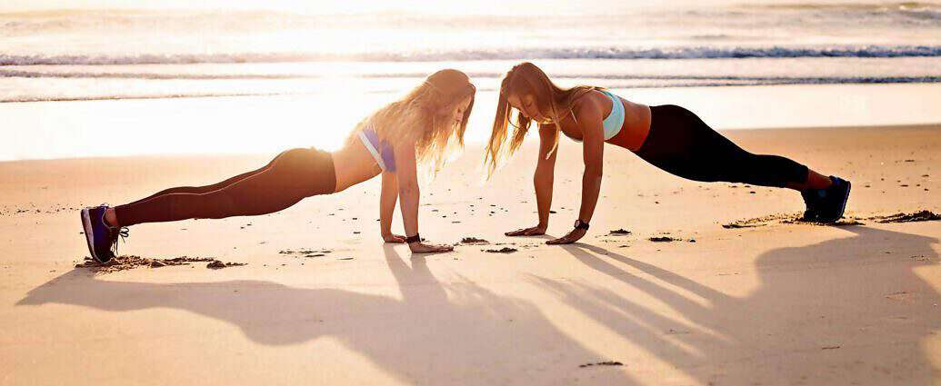 Zwei sportliche junge Frauen machen Liegestütze am Strand.