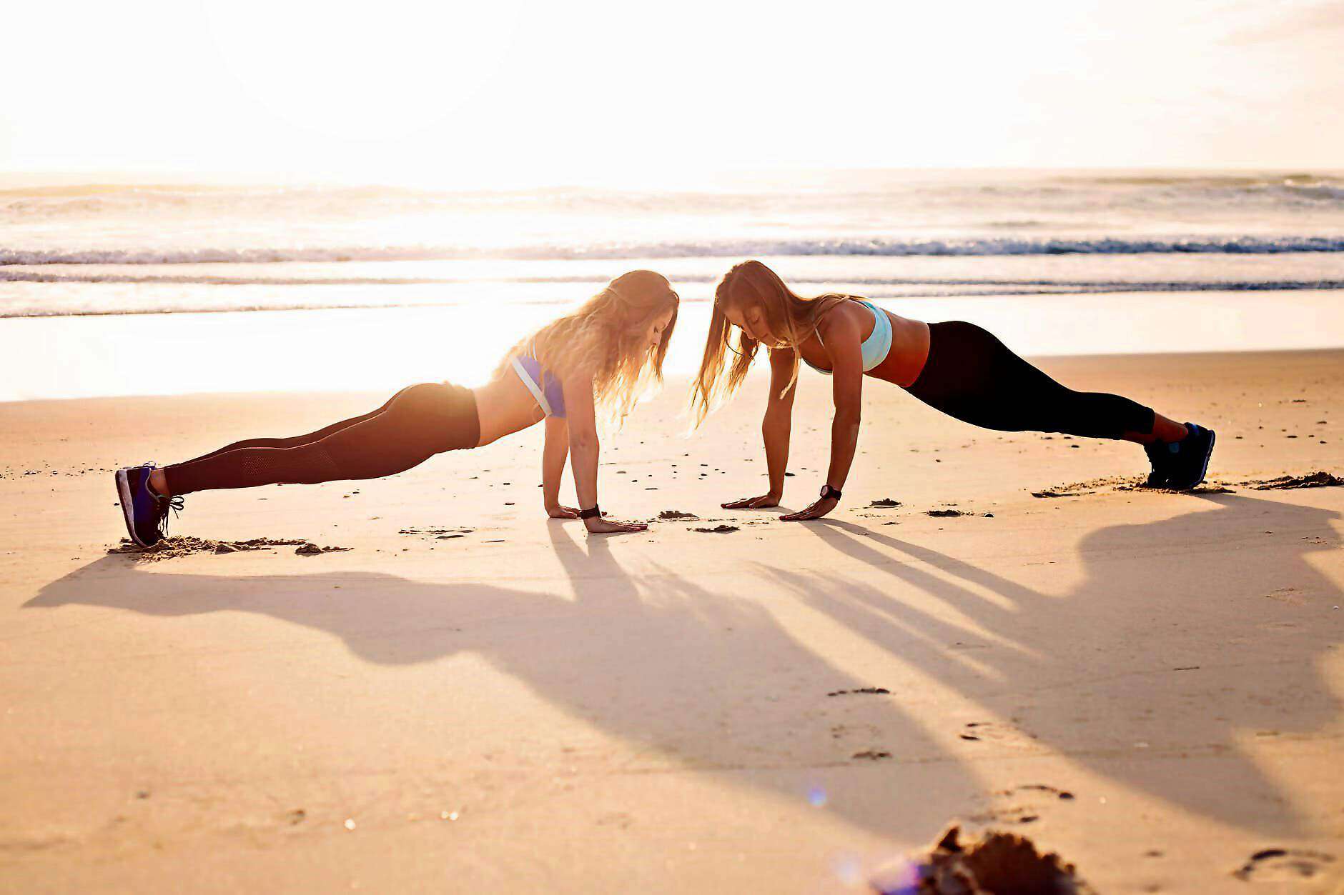 Zwei sportliche junge Frauen machen Liegestütze am Strand.