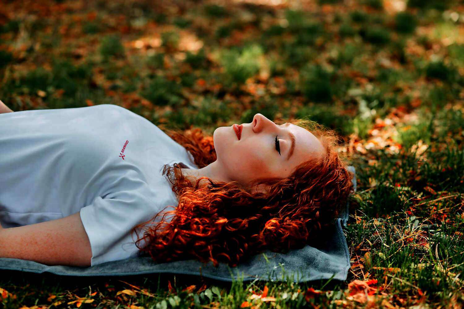 Eine junge Frau mit roten Haaren liegt verträumt mit geschlossenen Augen auf dem Boden.