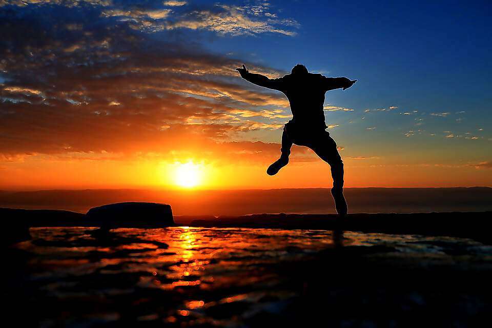 Ein junger Mann springt bei Sonnenuntergang am Meer in die Luft.