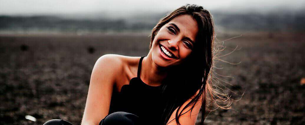 Eine schöne junge Frau steht in einer Landschaft und lacht fröhlich.