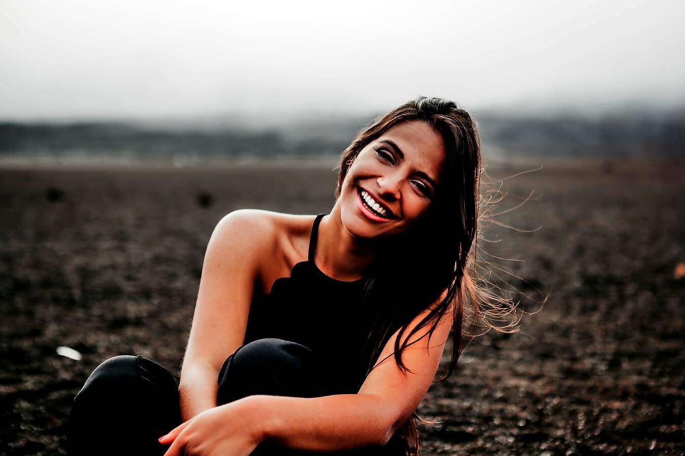 Eine schöne junge Frau steht in einer Landschaft und lacht fröhlich.