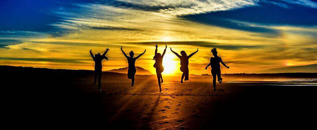 Vier Schatten junger Menschen, die vor einem Sonnenuntergang stehen und ihre Arme in die Luft strecken.