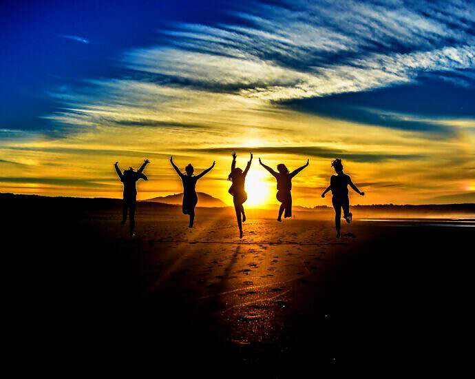 Vier Schatten junger Menschen, die vor einem Sonnenuntergang stehen und ihre Arme in die Luft strecken.