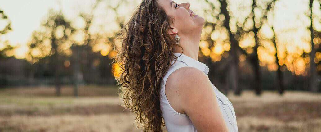 Eine junge Frau steht am Rande eines Feldes und lacht.