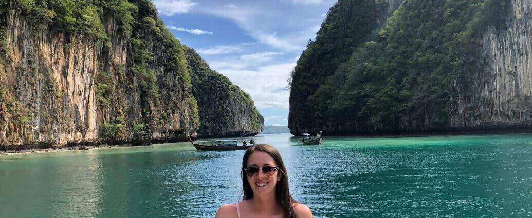 Ein Bild von einer jungen Frau in einem weißen Bekini auf einem kleinen Boot in Thailand, auf dem Meer, im Hintergrund die schönen Felsen im Wasser.