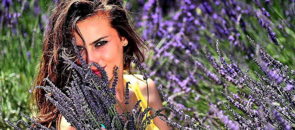 Eine junge Frau inmitten eines Lavendelfeldes und sie lacht vor Freude.