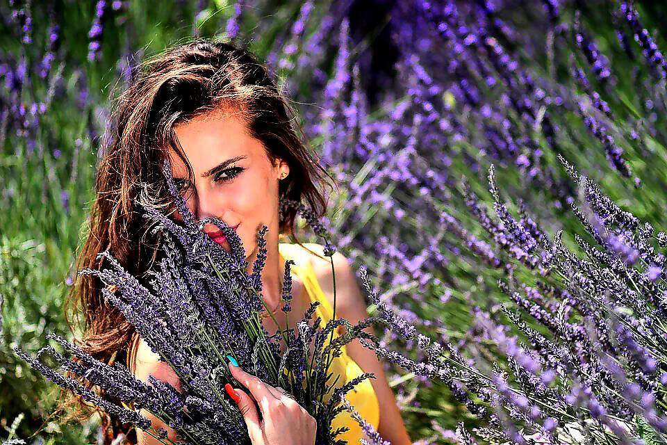 Eine junge Frau inmitten eines Lavendelfeldes und sie lacht vor Freude.