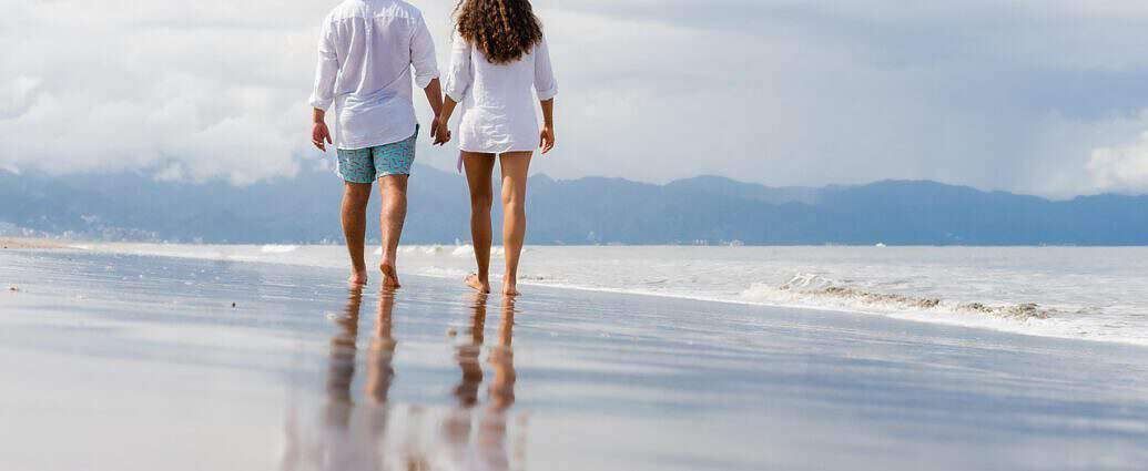 Ein junges Paar spaziert Hand in Hand am traumhaften Strand entlang.