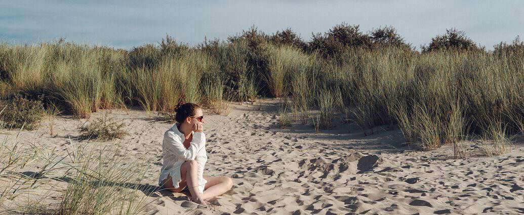 Eine junge Frau sitzt auf einer Düne am Strand.