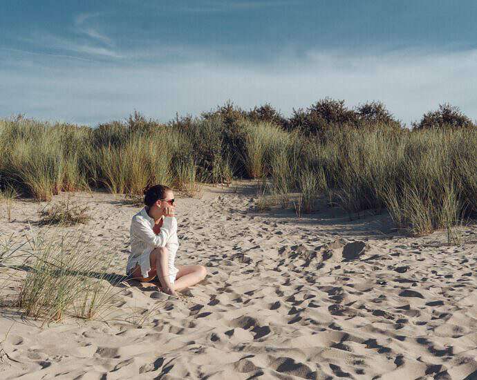 Eine junge Frau sitzt auf einer Düne am Strand.