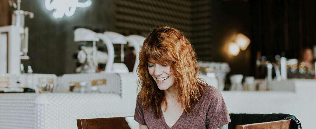 Eine hübsche Frau sitzt an ihrem Schreibtisch und lacht über ihren Laptop.