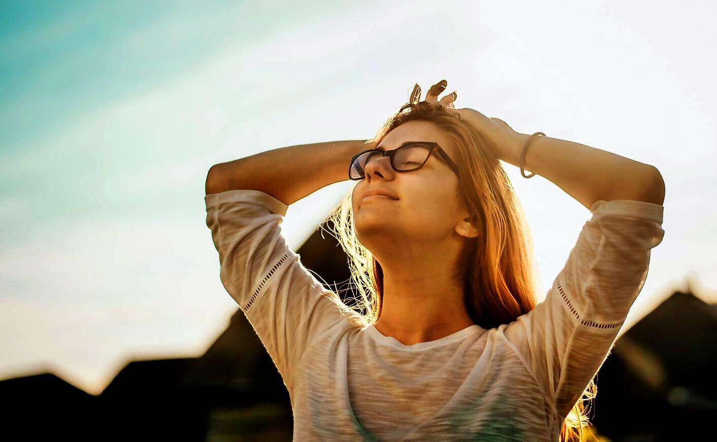 Eine junge Frau mit Brille hat die Arme nach hinten verschränkt und den Kopf zum Himmel erhoben.