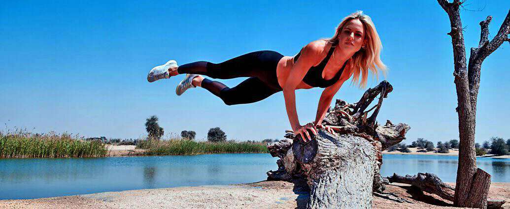 Eine junge, sportliche Frau schwingt sich kraftvoll an einem Baumstamm hinab. Sie trägt enge Sportkleidung.
