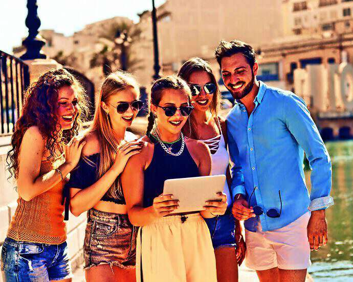 Freudig schauen junge Menschen auf ein Tablet und lachen, weil sie ihr Leben so gestalten können, wie sie es wollen.