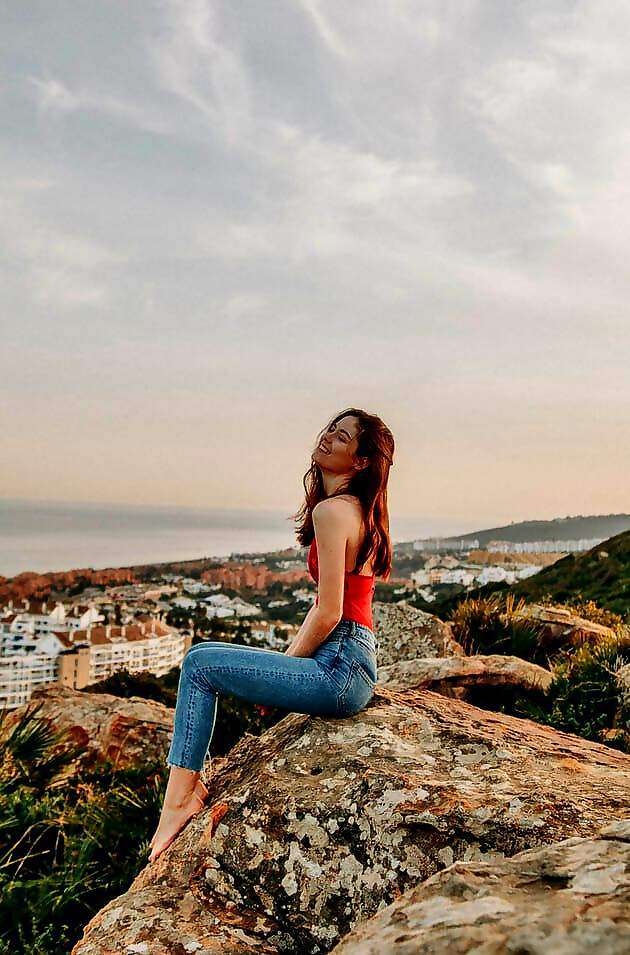 Eine junge Frau sitzt entspannt auf einem Felsen und schaut auf das Meer.