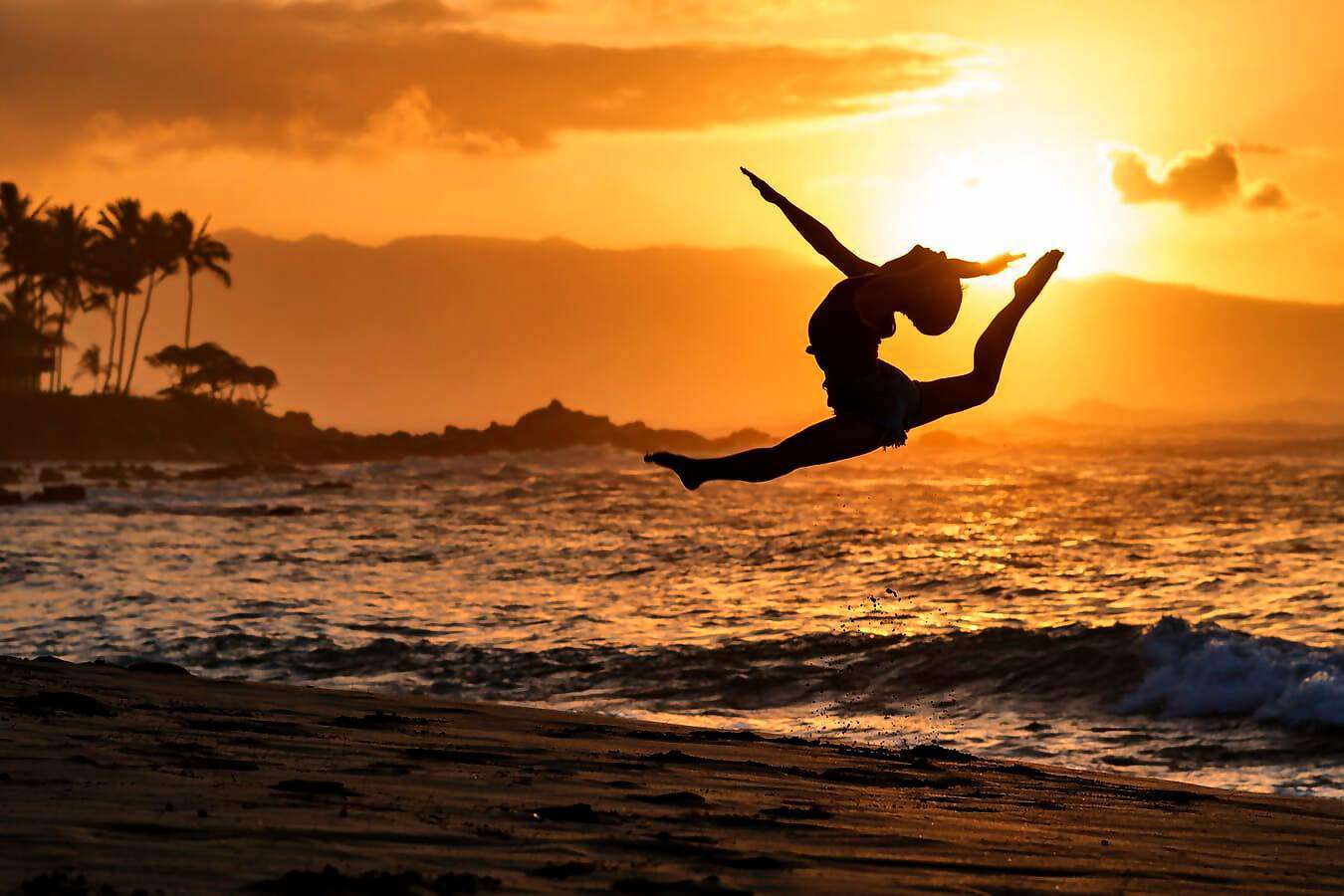 Eine junge Frau springt am Ufer des Meeres in die Luft und streckt dabei die Arme aus.