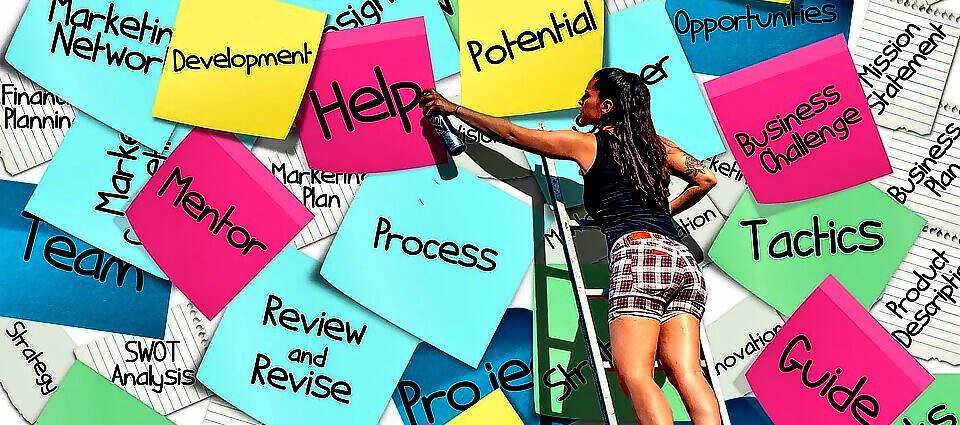 Eine junge Frau steht auf einer Leiter und bringt große Sticker auf eine Leinwand an.