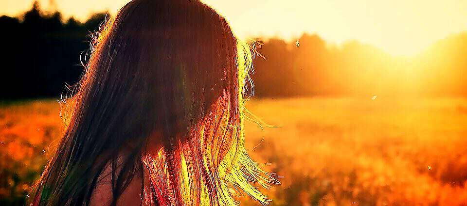 Eine junge Frau steht bei Sonnenuntergang in einem Blumenfeld und schaut nachdenklich.