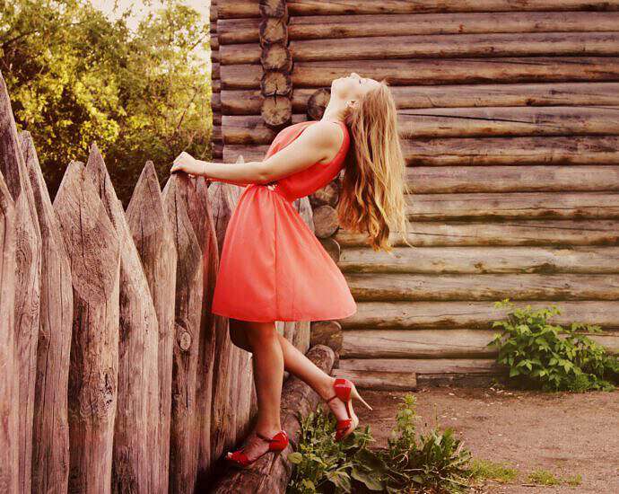 Eine junge Frau in einem roten Kleid steht verträumt an einem Zaum.