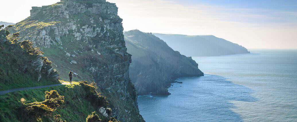 Eine junge Frau joggt einen Felspfad entlang. Unter ihr liegt das Meer.