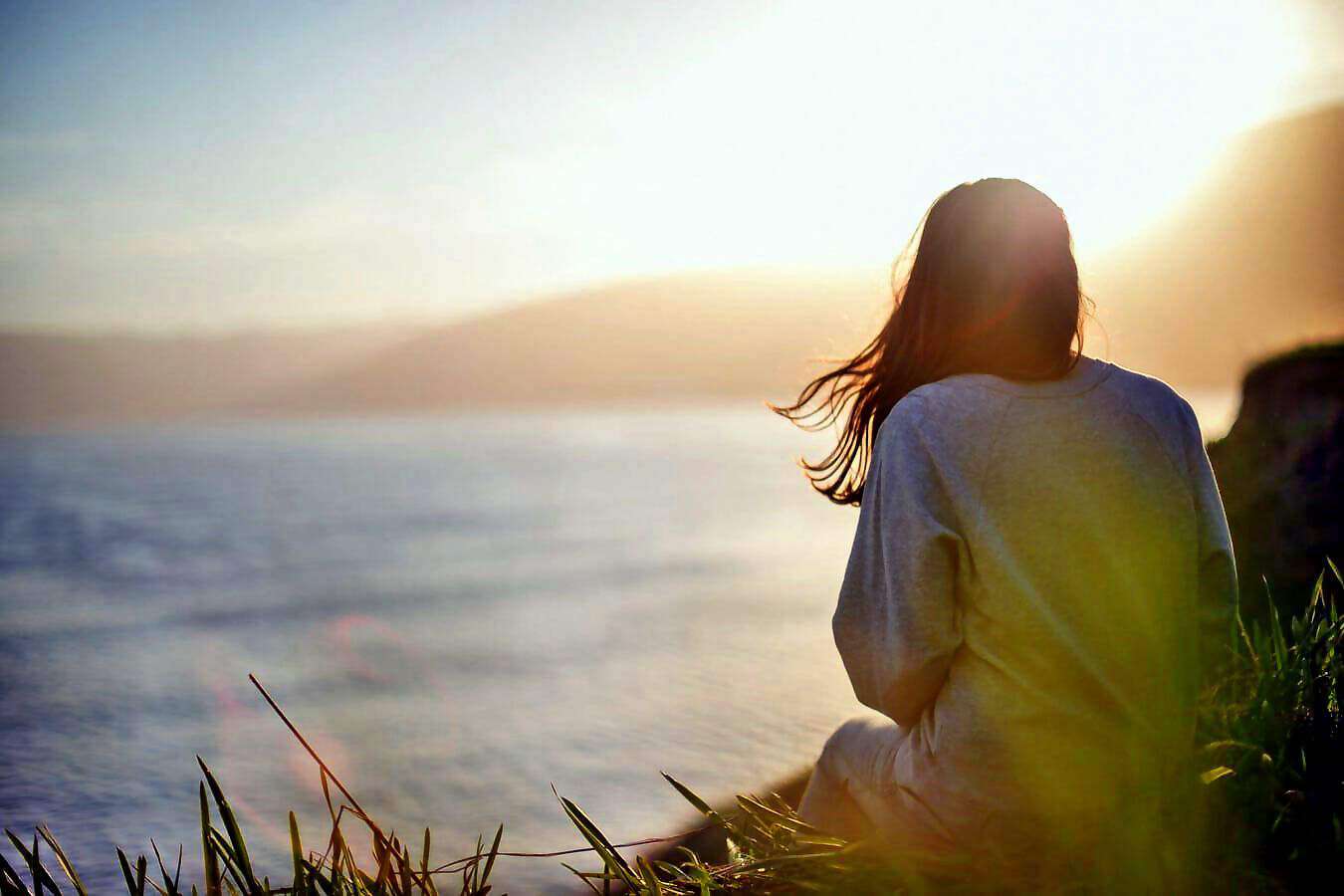 Eine junge Frau sitzt in der Abendsonne am Berghang.