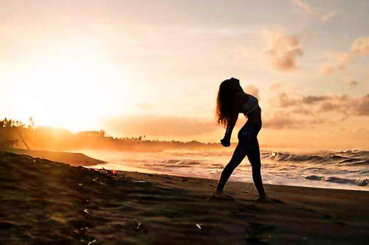 Eine junge Frau rekelt sich bei Sonnenuntergang am Meer.