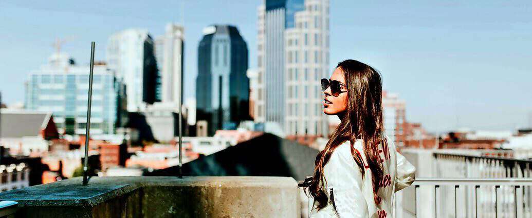 Eine junge Managerin steht mit Sonnenbrille in einer schönen Stadt.