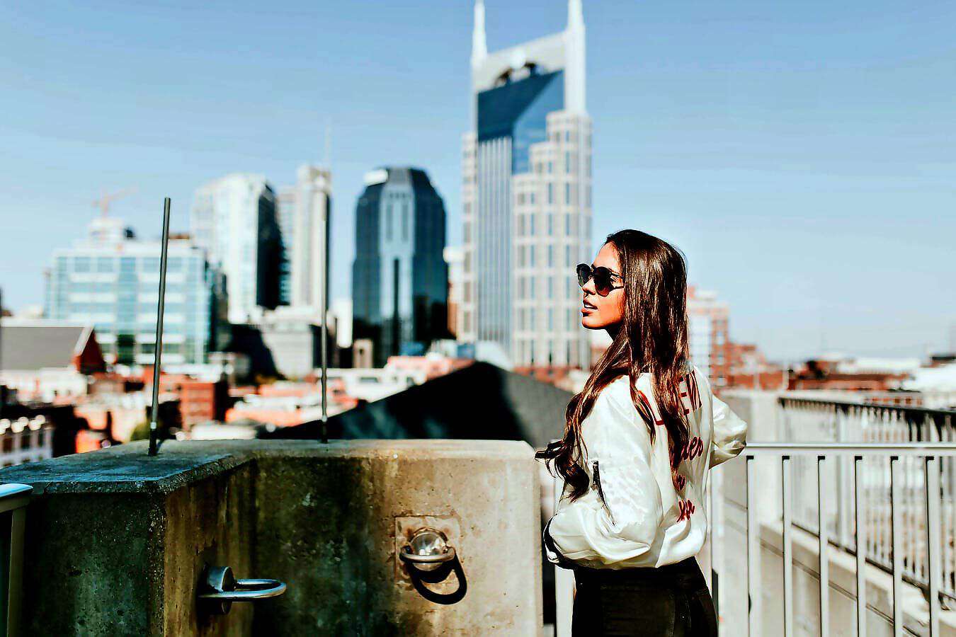Eine junge Managerin steht mit Sonnenbrille in einer schönen Stadt.