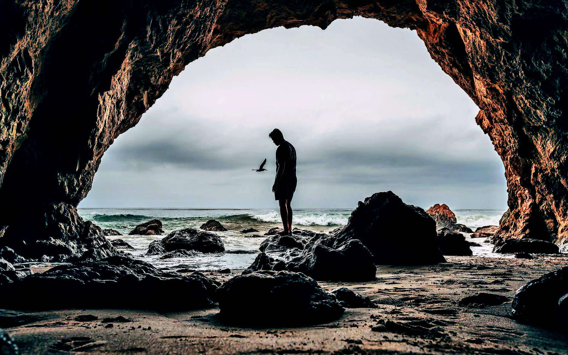 Ein Mann steht verträumt am Meer, vor ihm ein Felsbogen.