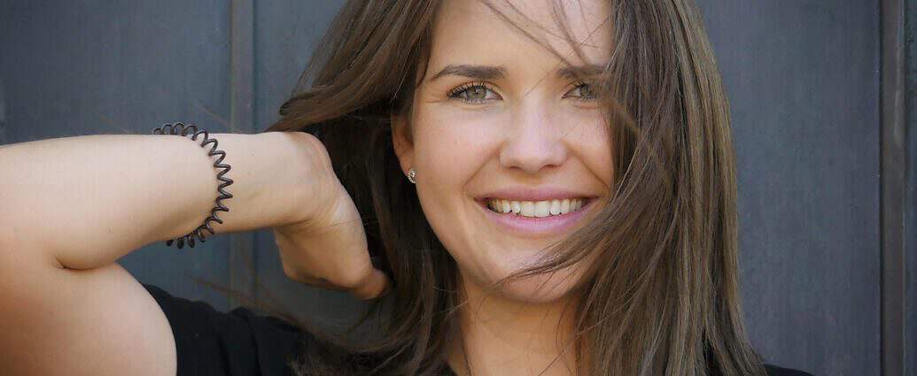 Eine junge Frau mit langen braunen Haaren lächelt freudig.