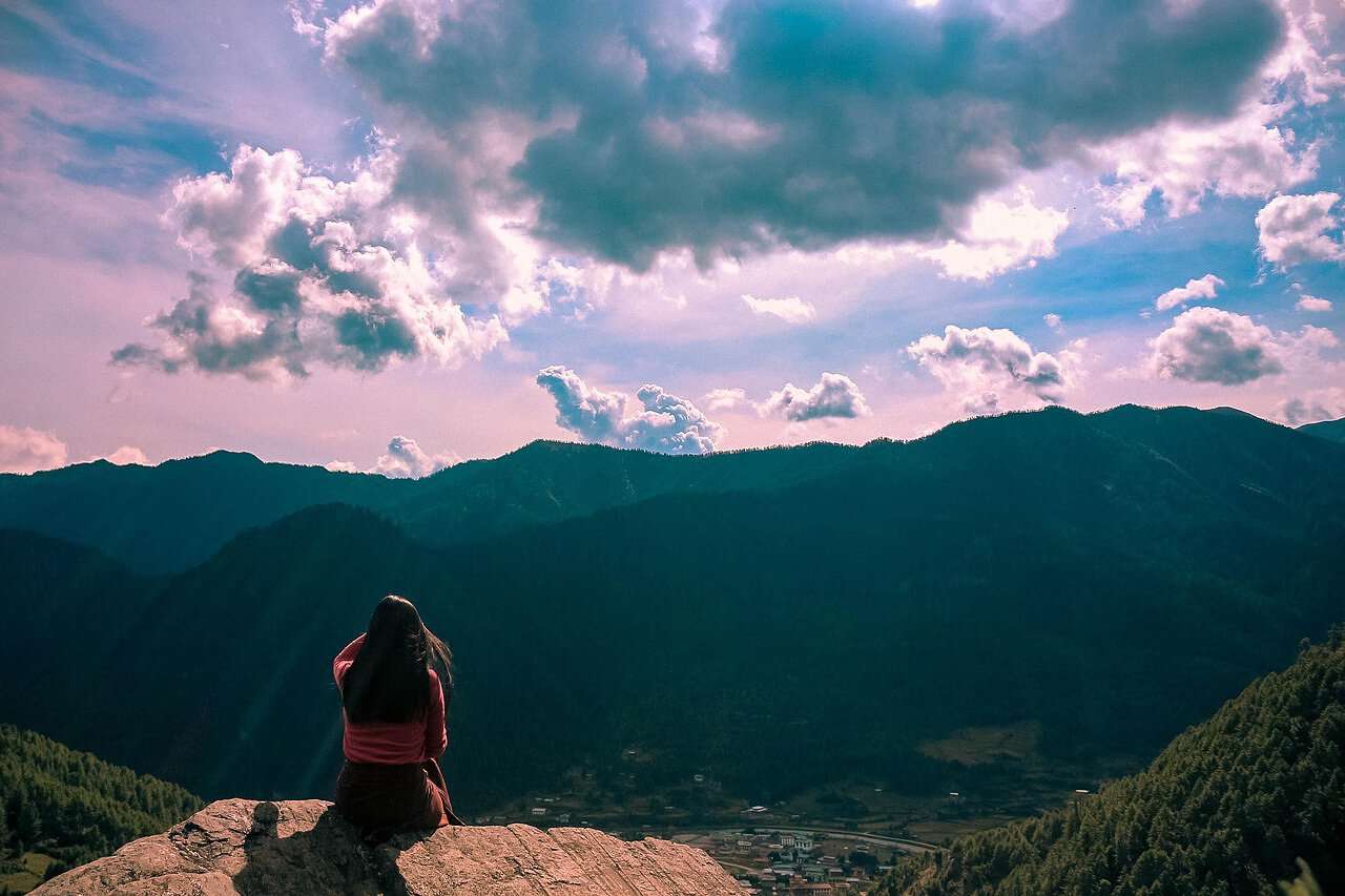 Eine junge Frau sitzt am Berghang und blickt auf die Berge Bhutans.