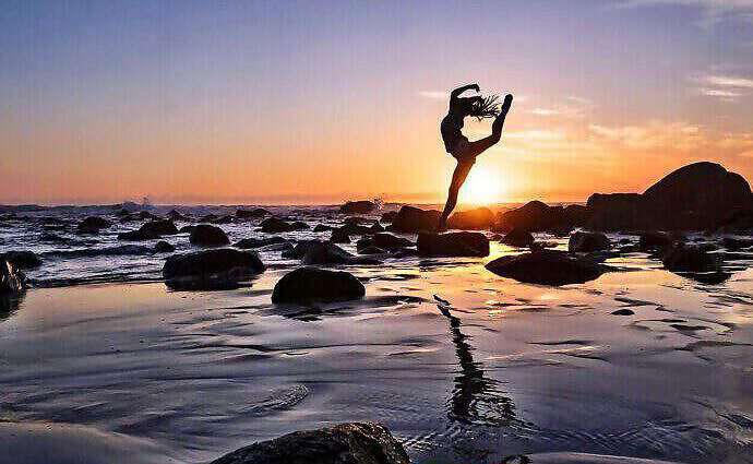Eine junge Frau springt vor Freude im Sonnenuntergang am Strand in die Luft.