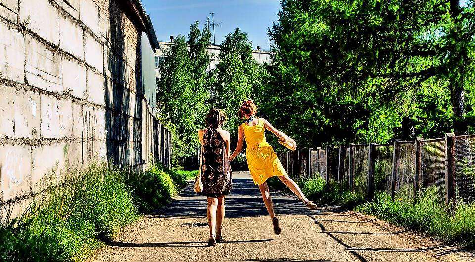 Zwei Frauen sind auf einem Weg unterwegs. Eine der Frauen springt seitlich zur Seite etwas hoch.