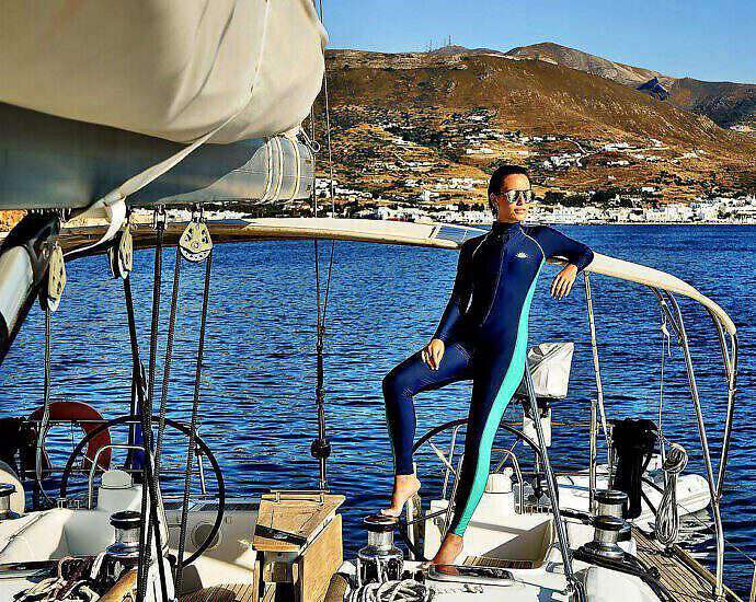 Eine junge Frau mit einem Neoprenanzug steht locker und gelassen auf einem schönen Boot.