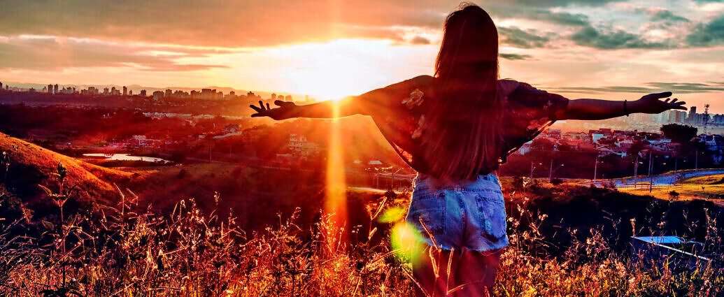 Eine junge Frau steht zum Sonnenuntergang und streckt die Arme aus.