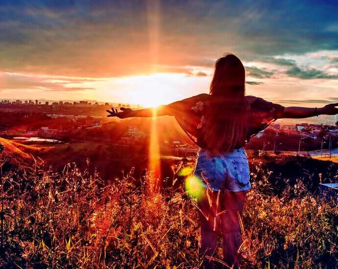 Eine junge Frau steht zum Sonnenuntergang und streckt die Arme aus.