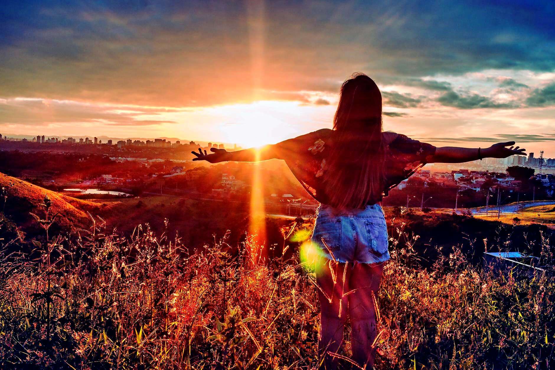 Eine junge Frau steht zum Sonnenuntergang und streckt die Arme aus.