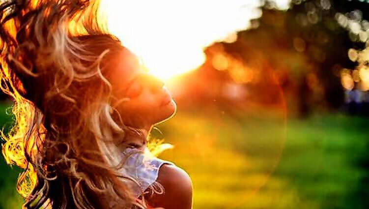 Eine schöne, junge Frau blickt verträumt in die Abendsonne, während der Wind durch ihr Haar streift.