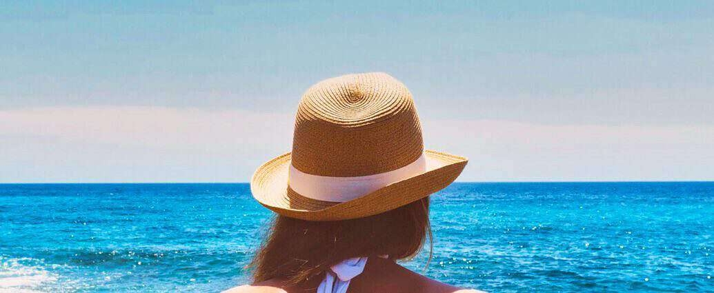 Eine junge Frau mit Strohhut schaut aufs Meer.