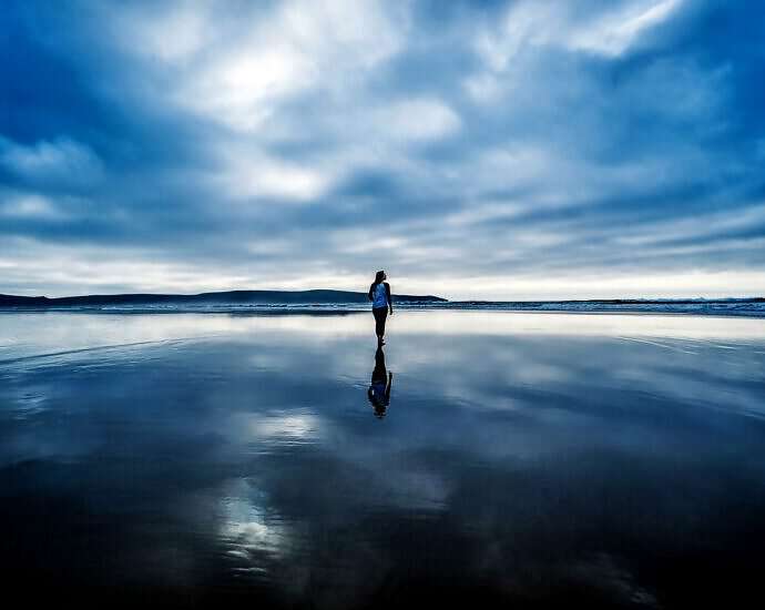 Eine junge Frau geht in der Morgendämmerung am seichten Meeresufer spazieren.