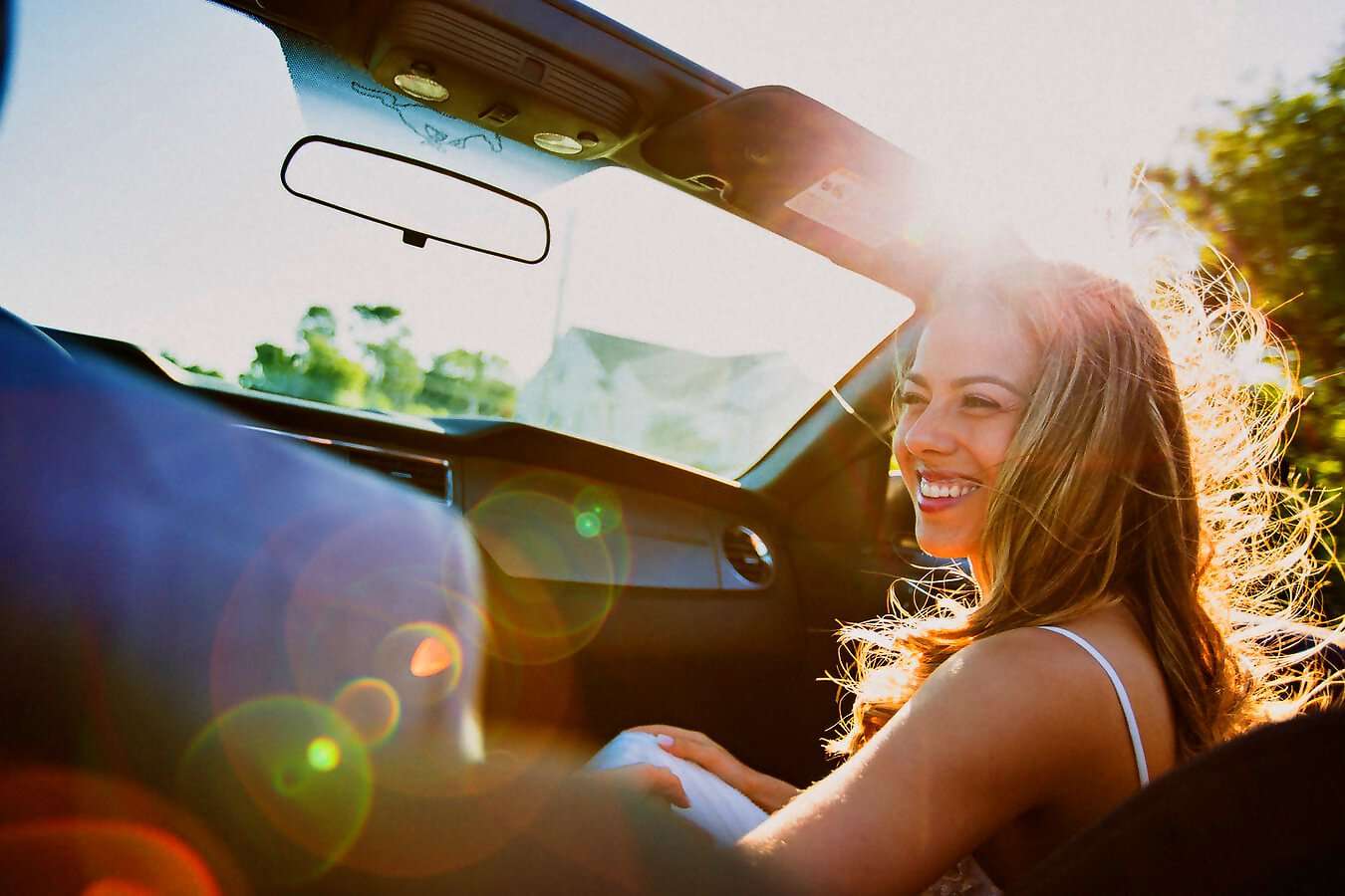 Eine schöne, junge Frau sitzt als Beifahrerin im Auto und lacht herzlich.