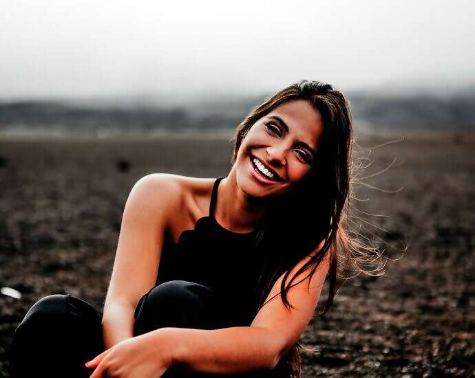 Eine junge Frau mit langen braunen Haaren lacht fröhlich.