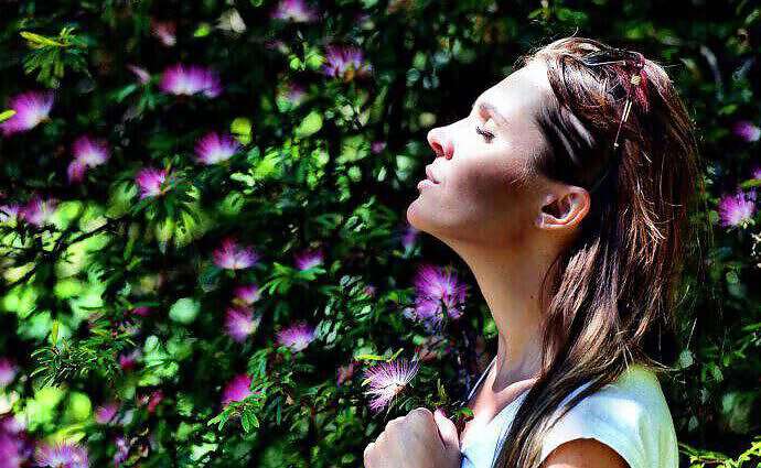 Eine junge Frau, die tief und entspannt in einem Blumengarten atmet.