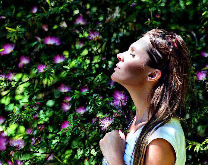 Eine junge Frau, die tief und entspannt in einem Blumengarten atmet.