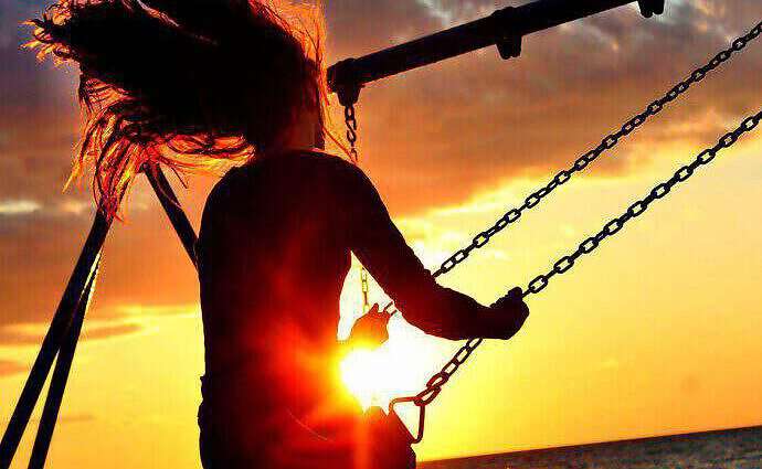 Eine junge Frau schaukelt dem Sonnenuntergang entgegen.